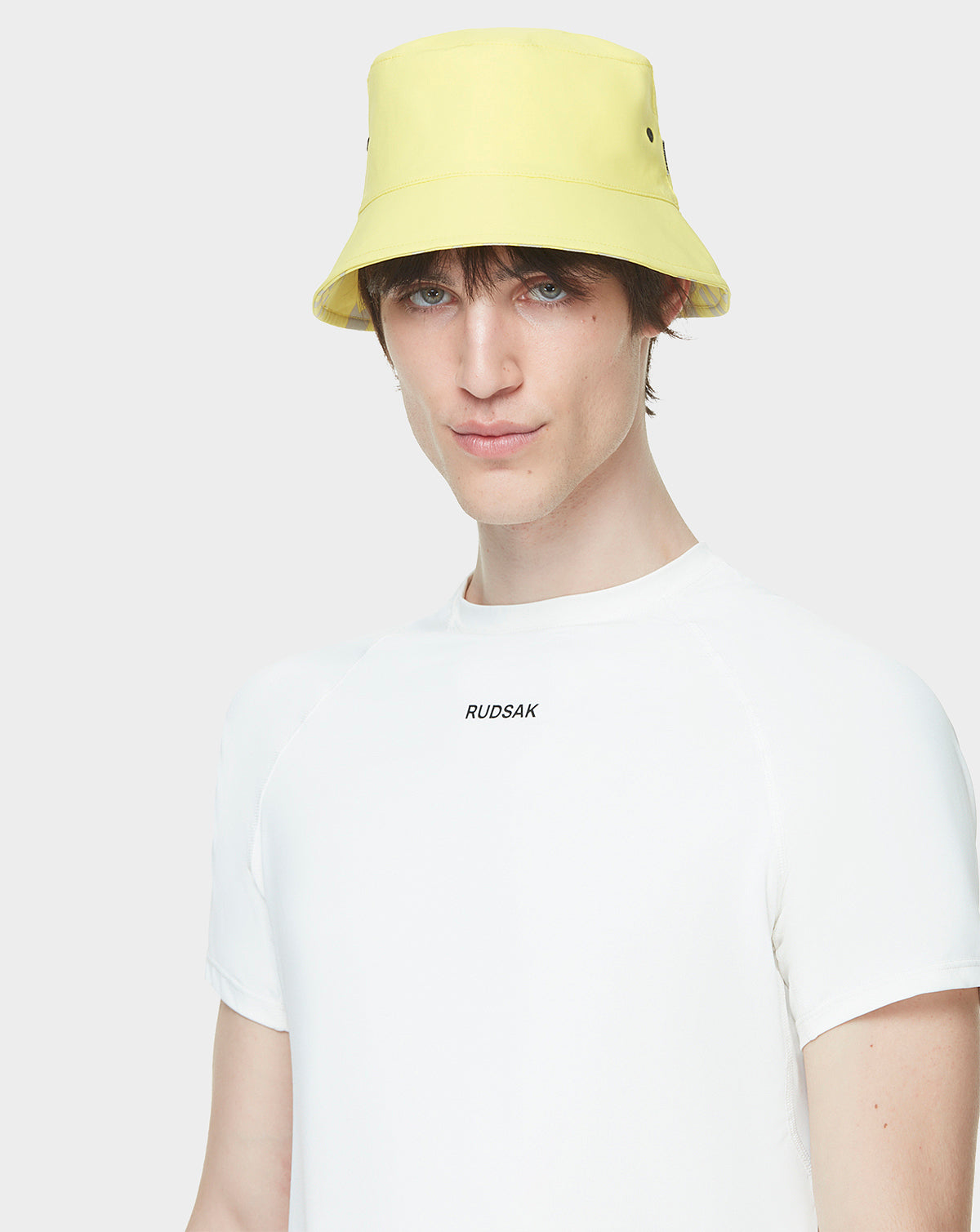A young person wears the AYLA - 9422004 YELLOW reversible bucket hat and a white Rudsak t-shirt with the brand logo, standing against a plain light background.