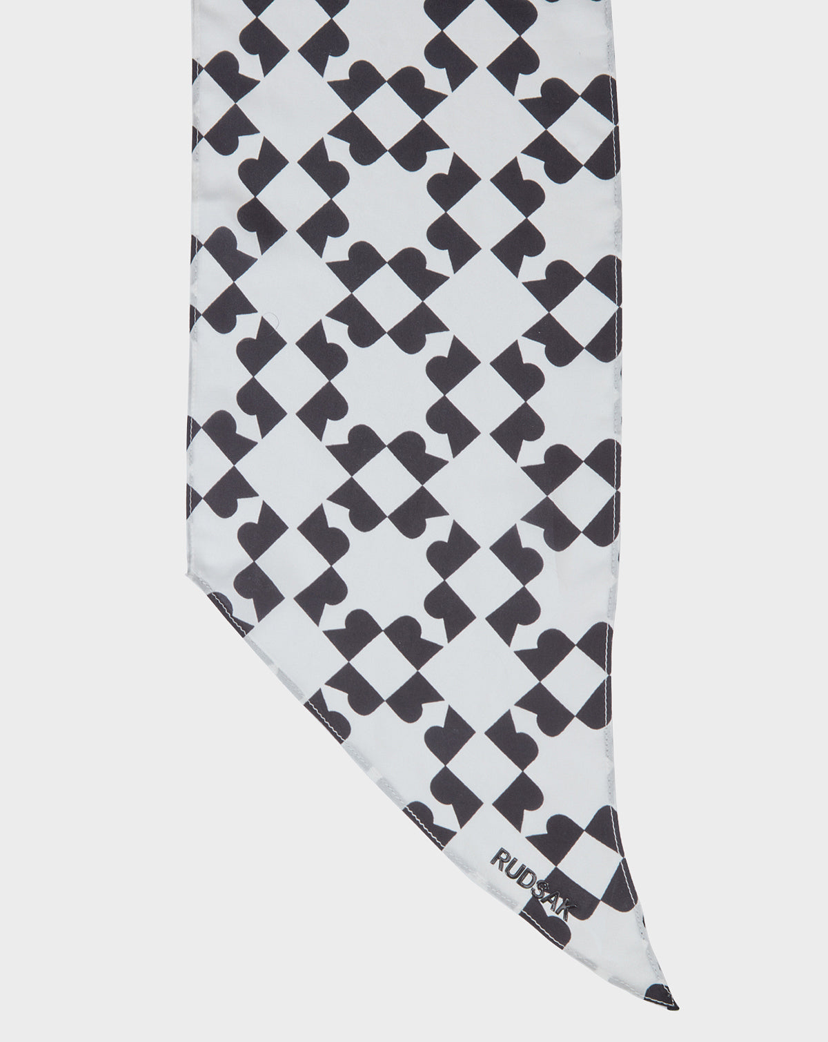 The ODELYA FINAL SALE - 8422001 WHITE by Rudsak is a lightweight silk women’s scarf with a unique repeating black geometric print, diagonal edge, and the Rudsak brand name printed in black near the bottom corner.