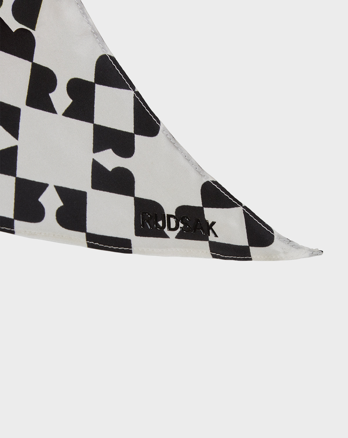 A close-up of the ODELYA FINAL SALE - 8422001 WHITE women’s silk scarf by Rudsak, featuring a black geometric heart pattern and “RUDSAK” stitched in black thread along the edge.